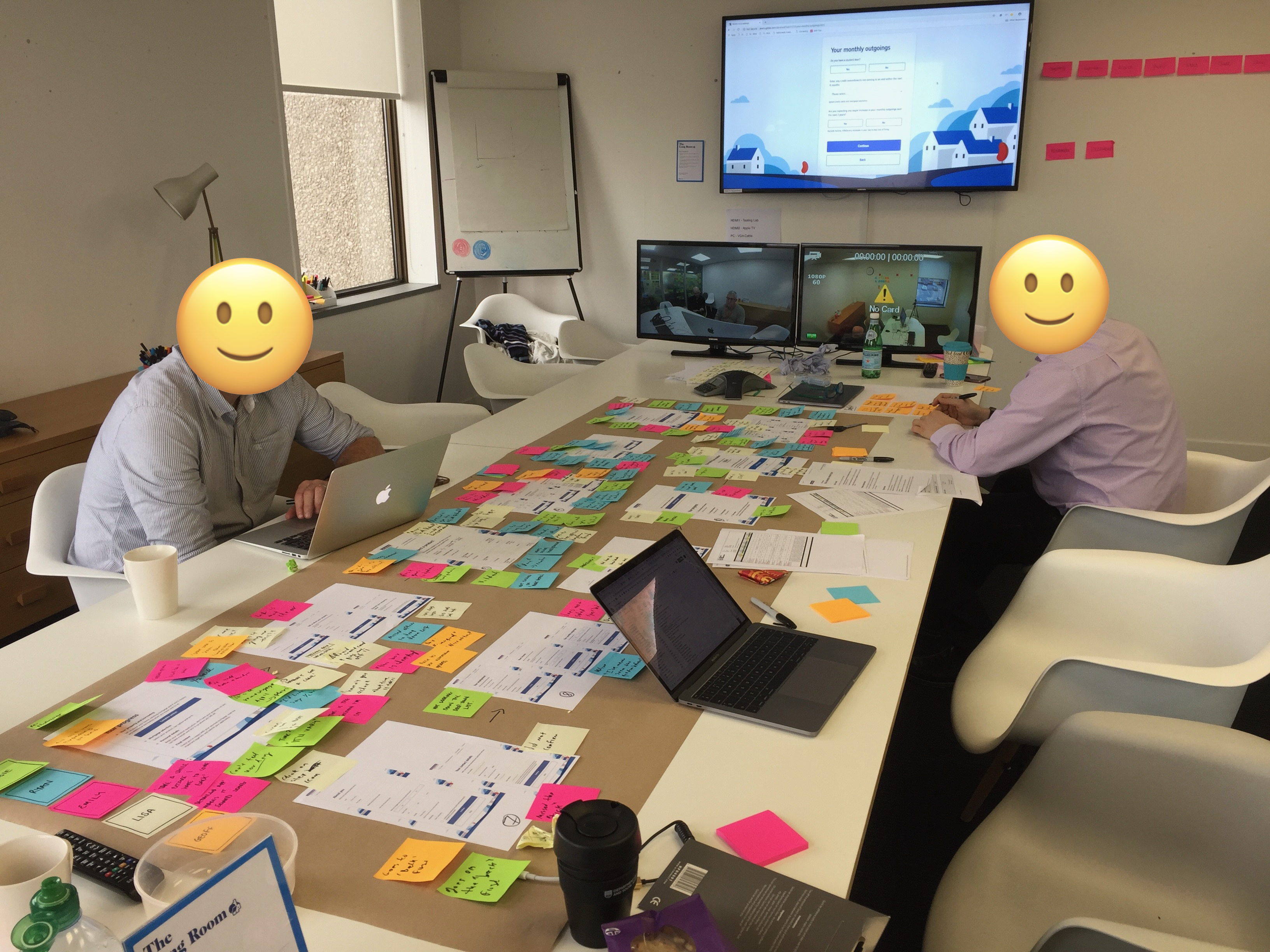 User testing session with a prototype on screen and journey artefacts spread across a table.